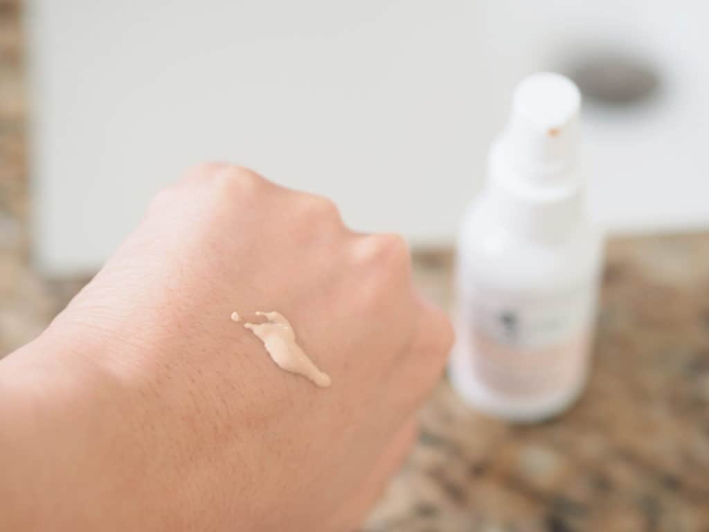 A woman's hand with a small amount of Blissoma's Photonic, a mineral sunscreen and moisturizer made from nontoxic and nourishing fresh ingredients, on top of it and the bottle in the background