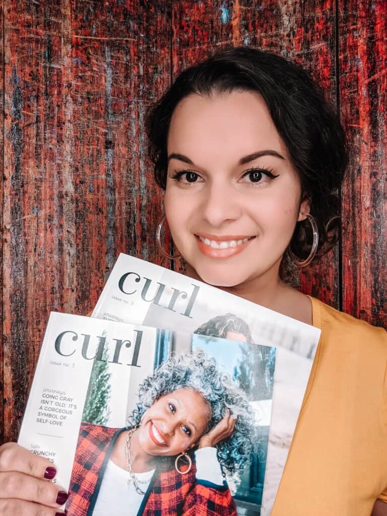 Delilah's curly hair in a loose low side bun holding Curl magazine