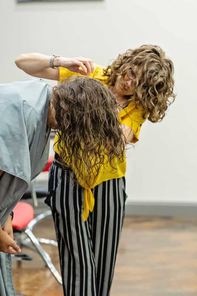 Laurie Cain Curl Specialist cut curly hair Holistic Enchilada team member client leaning forward while Laurie cuts her hair