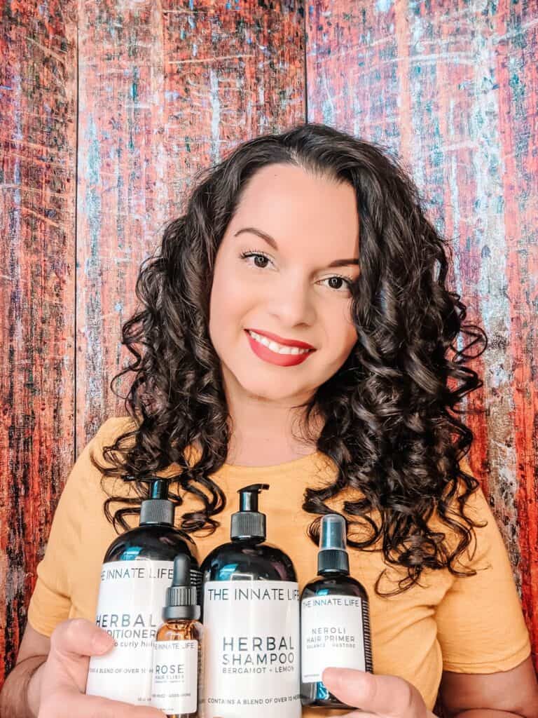 Delilah with perfect curls smiling and holding the innate Life line of products in her hands