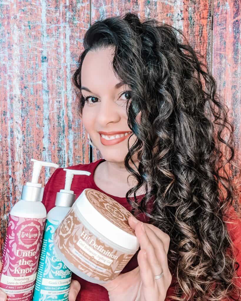 Delilah Orpi the holistic enchilada smiling and showing her curls while holding three TreLuxe hair products