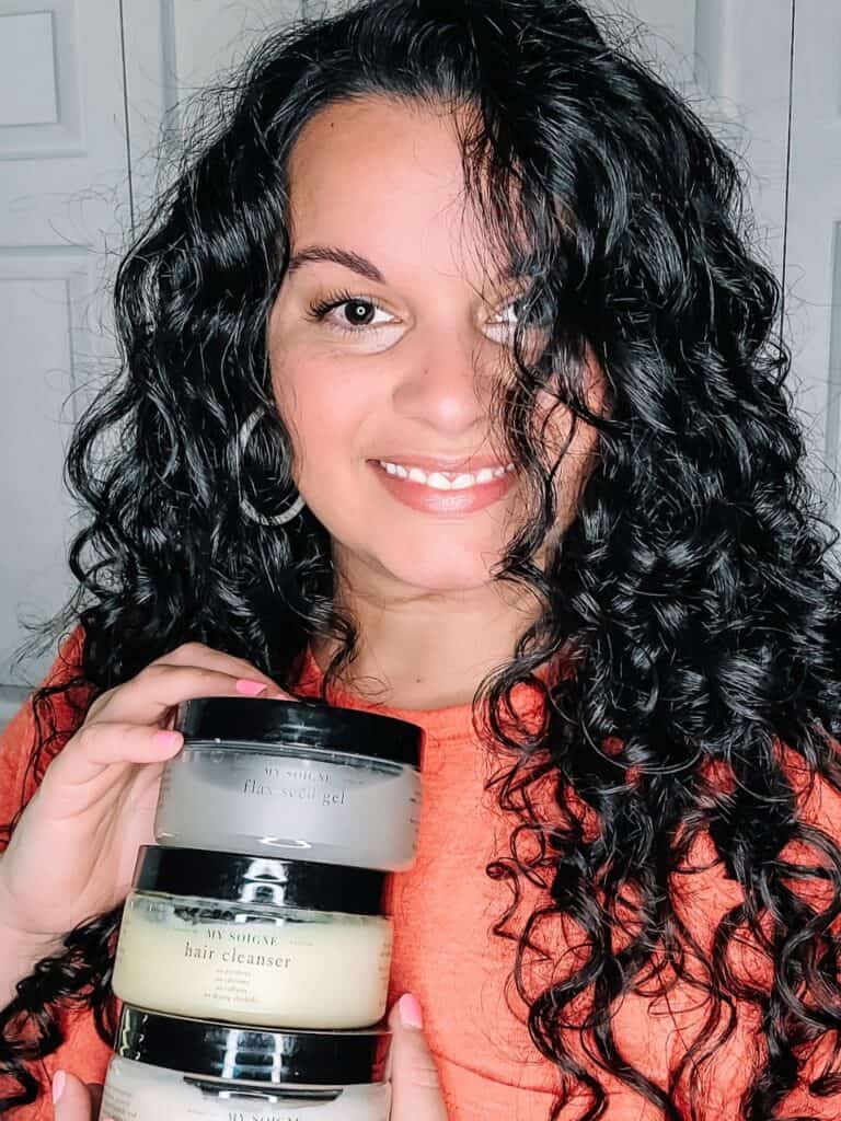 My Soigne Review - Delilah holding up My Soigne flaxseed gel, hair cleanser, and protein leave-in with styled hair