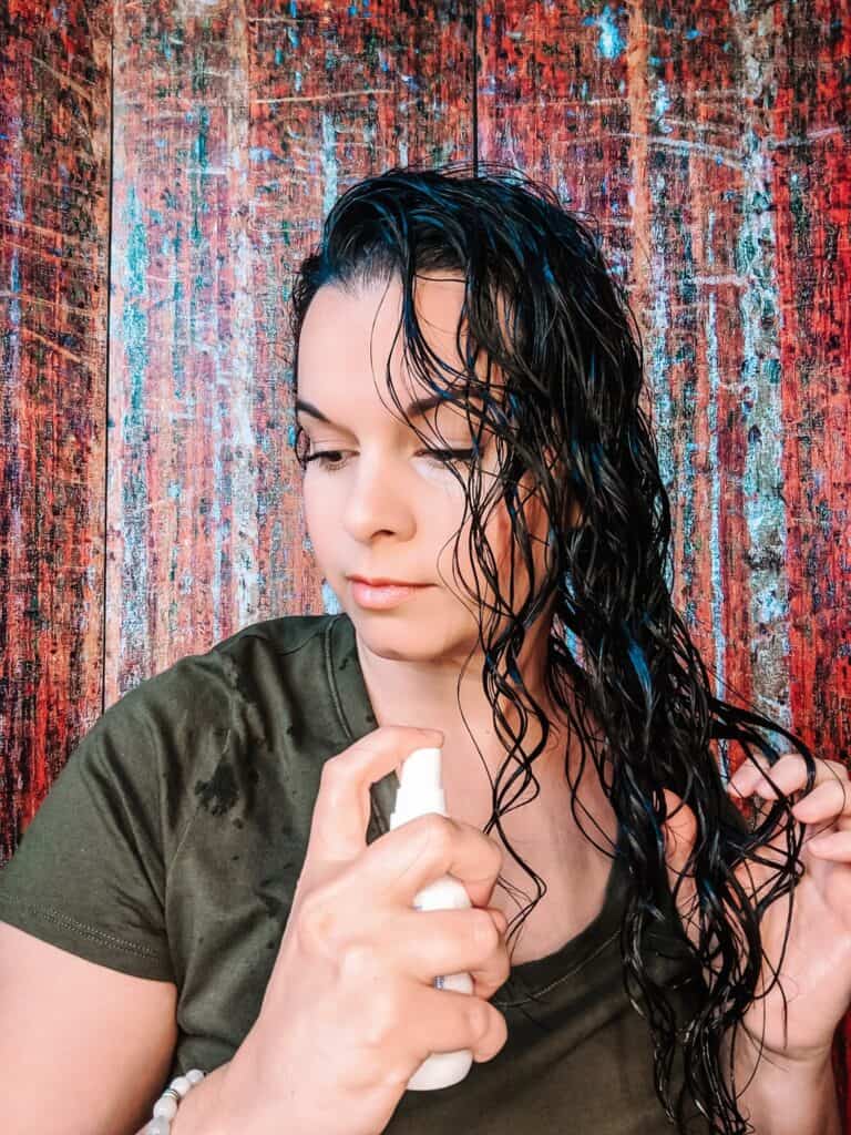 woman spraying detangling spray in wet hair to prevent matted hair
