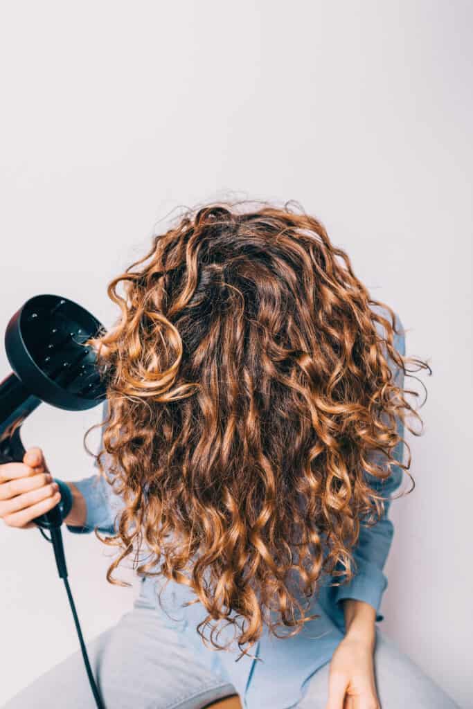 Close-up young woman sitting on chair styling her curly hair with a curly hair diffuser