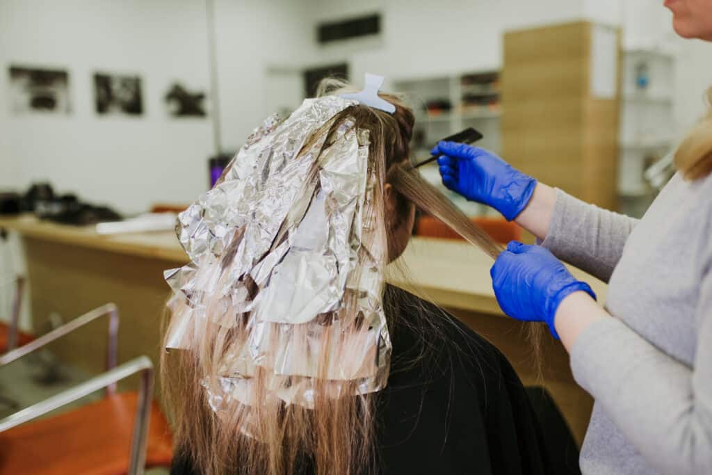 Hairdresser is dying female hair, making hair highlights to his client with a foil.