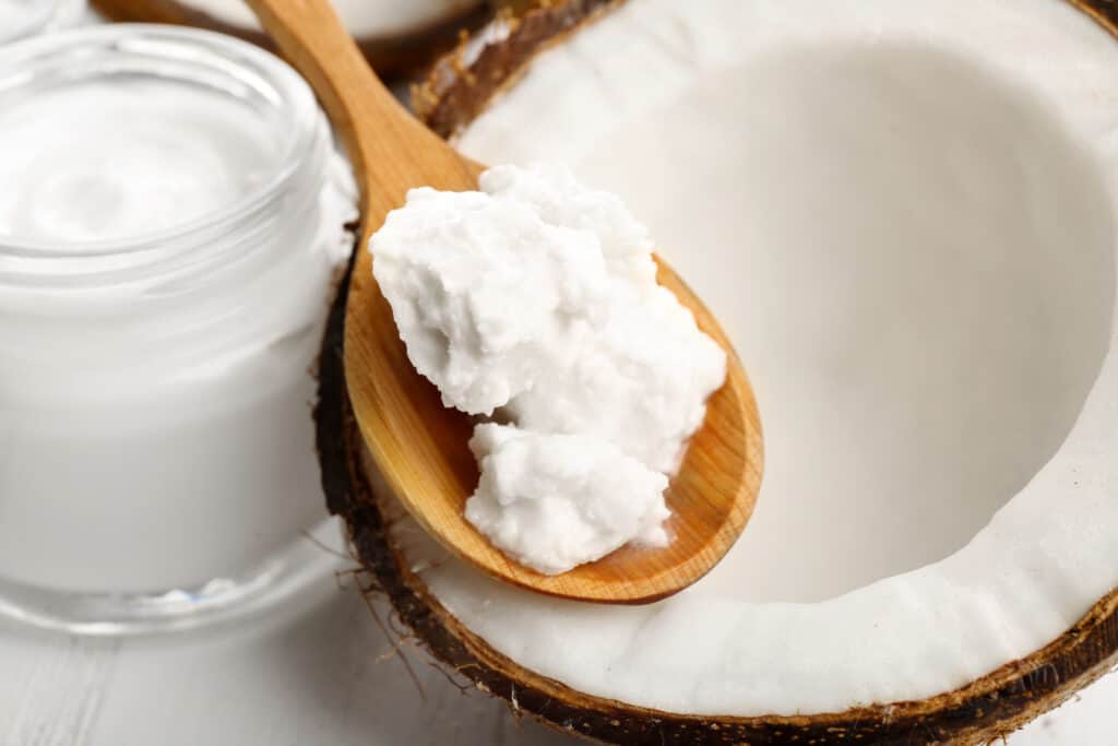 Coconut with coconut oil and jar of cosmetic cream on table close up