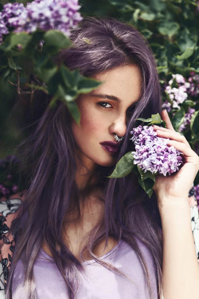 woman with long dark purple hair holding a purple flower against her face