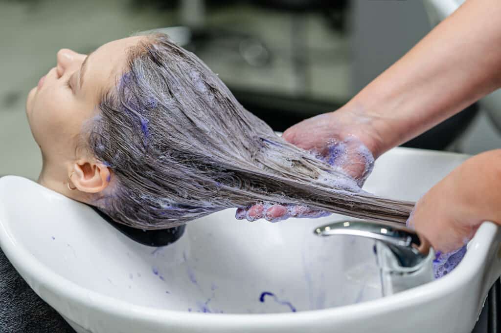 Hair stylist applying purple shampoo after hair lightening.