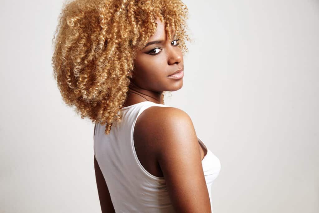black woman with blonde curly hair looking back