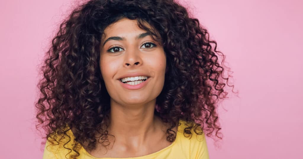 woman with 3b curly hair smiling in front of pink background