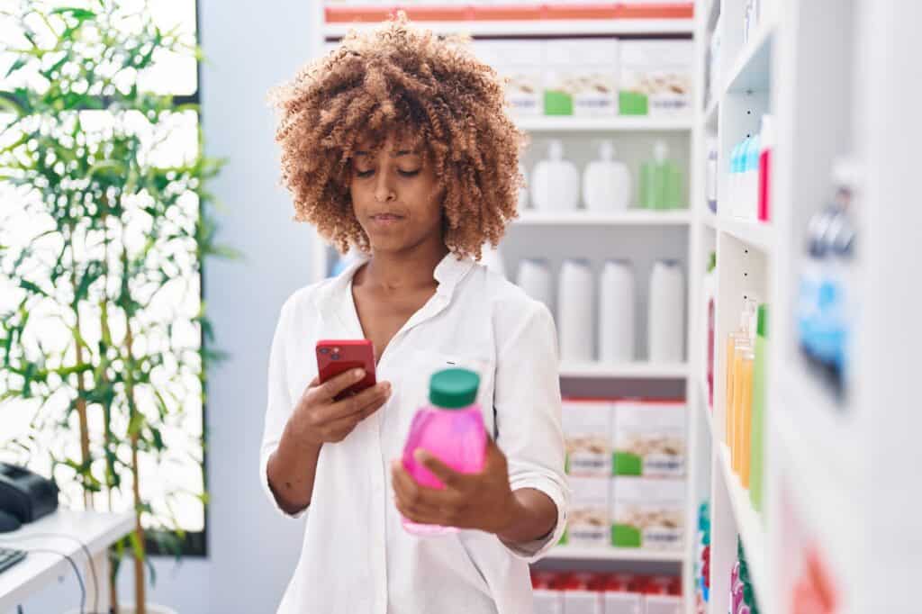 woman with curly hair looking at dandruff shampoos in store and searching something on her phone.